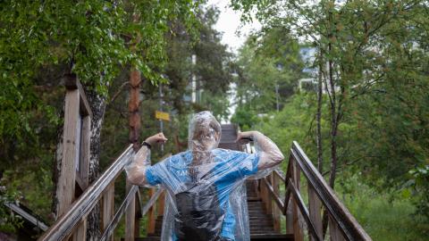 Henkilö portaiden alapäässä sadeviitta päällä. Henkilöllä on kädet ylhäällä ja hän jännittää hauiksiaan