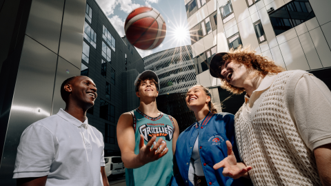 Four cheerful young people with a basketball outside the Nokia Arena.