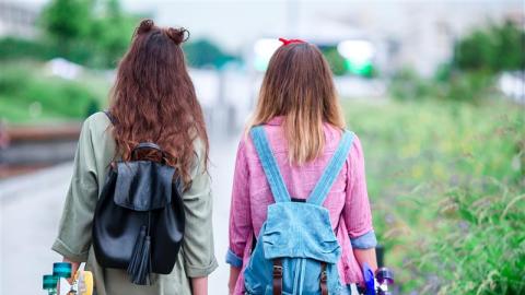 Kaksi nuorta kävelemässä poispäin katsojasta. Kummallakin on pitkät ruskeat hiukset ja kädessään skeittilauta.