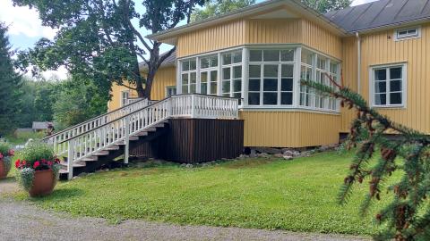 Keltainen kartanorakennus, jonka takana lasierkkeri.