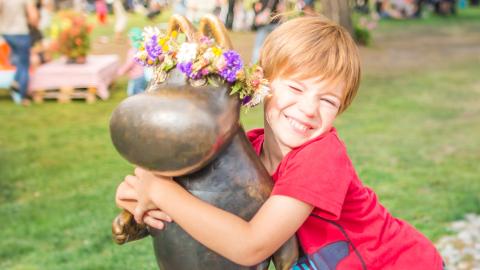 A boy hugging a statue of the Moomintroll, adorned with a floral headband, in Sorsapuisto Park, Tampere.