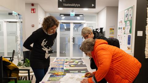 Kaupungin asiantuntija ja kaksi tamperelaista ovat kumartuneena yhdessä tutkimaan pöydällä olevaa asiakirjaa.