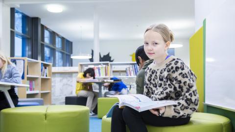 Nuori oppilas istuu kirja sylissä koulun tiloissa.