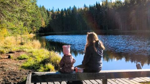 Lapsi ja nainen istuvat auringossa laiturin penkillä katsellen järvelle.