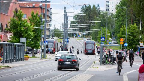Henkilöautoja, ratikoita, pyöräilijöitä ja kävelijöitä Hervannan keskustassa.