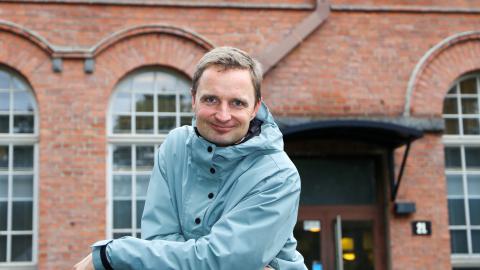 Mikko katsoo suoraan kameraan taustallaan Frenckellin punatiilinen rakennus.