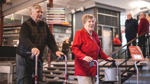 Mies ja nainen kävelevät rollaattoreista tukea ottaen.