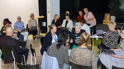 Monta henkilöä istuu juttelemassa eri ryhmissä.