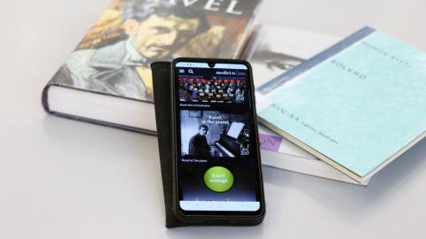 Älypuhelin nojaa kirjapinoon. Puhelimen näytöllä on avoinna videopalvelu, jossa voi katsoa konsertteja.