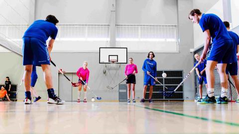 Lukio-opiskelijat pelaavat salibandya koulun liikuntasalissa. 