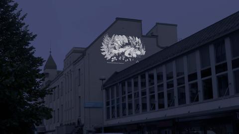 Havainnekuva katunäkymästä, jossa talon seinälle on heijastettu muumikuvitus.