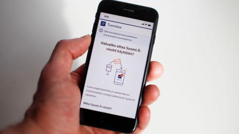 Ihmisen kädessä matkapuhelin, jonka näytöllä ohjeistetaan, miten voi ottaa käyttöönsä suomi.fi-viestit.