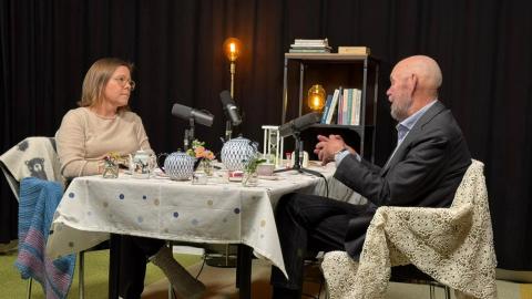 Nainen ja mies keskustelevat teepöydän ympärillä podcast-lavasteissa. 