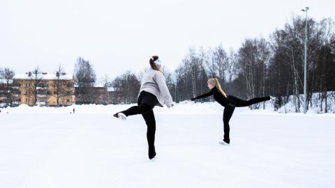 Kaksi tyttöä luistelee ulkokentällä.