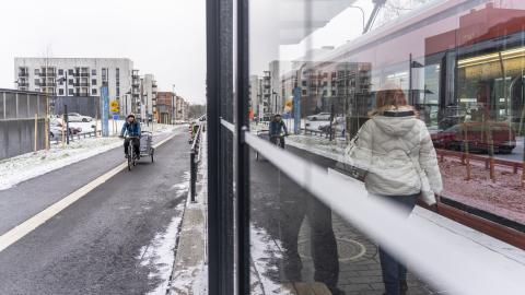 Pyöräilijä ja pyörän vetokärry lähestyvät ratikkapysäkkiä yhtä aikaa ratikan kanssa Hervannassa.