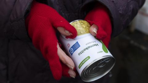 Hernekeittopurkki ja ihmisen kädet, joissa on punaiset rikkinäiset kangashansikkaat.