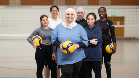 Kuusi naista lentopallokentällä ryhmäkuvassa. Kolmella heistä on lentopallo kädessään. 