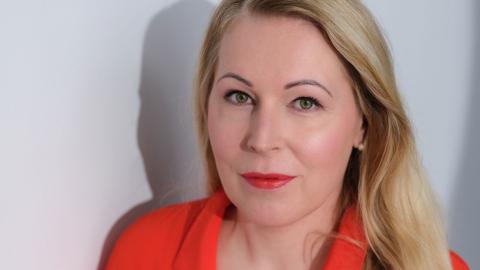 Irene katsoo suoraan kameraan kirkkaanpunainen paita päällään.