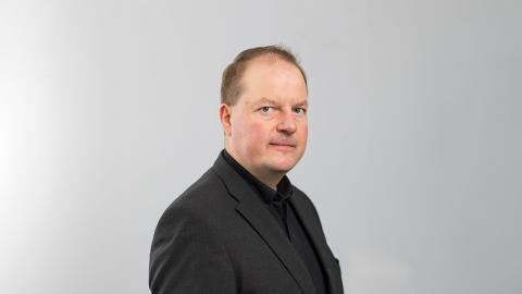 Mustaan pikkutakkiin pukeutunut Ari katsoo suoraan kameraan.