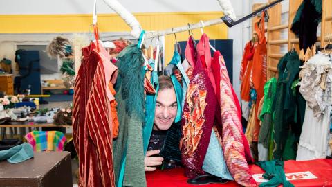 Mies kurkistaa värikkäiden vaatteiden välistä.