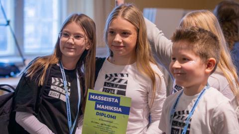 Kolme nuorta poseeraa kameralle diplomi kädessään
