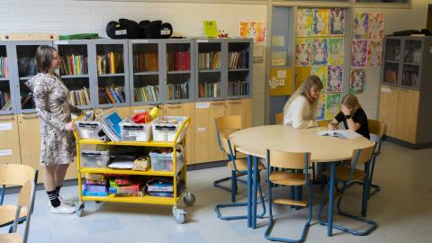 Kaksi opettajaa auttaa oppilasta läksyjen kanssa koulussa.