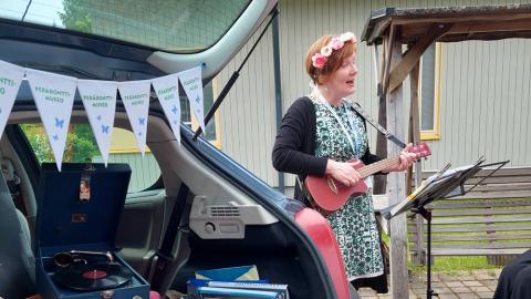 Nainen soittaa ukulelea kukkaseppele päässään ja laulaa yleisölle.