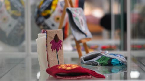 Vitriini, jossa on kirjontatöitä. Etualalla kukka-aiheinen työ.