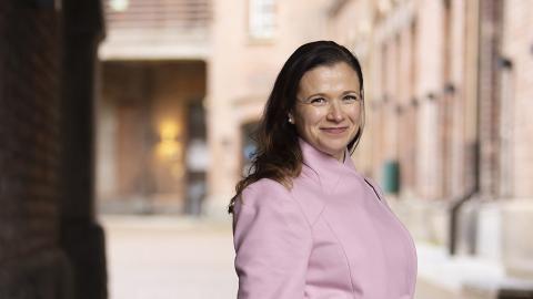 Maria Nikkilä katsoo hymyillen kameraan päällään vaaleanpunainen villakangastakki. 