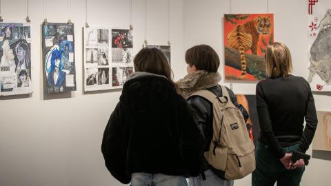 Kolme henkilöä katsoo näyttelyä galleriassa