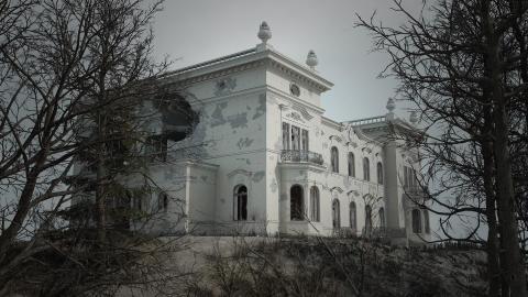 Milavidan valkoinen palatsi pommitusten jäljiltä, edessä lehdettömiä puita.
