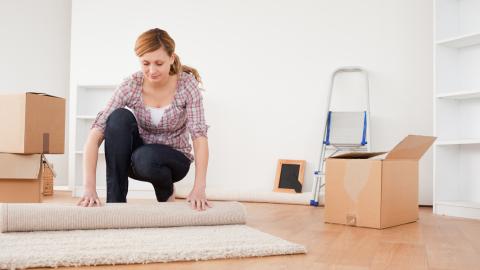 Nainen käärii mattoa rullalle ja vieressä on pahvilaatikkoja sekä tikapuut.