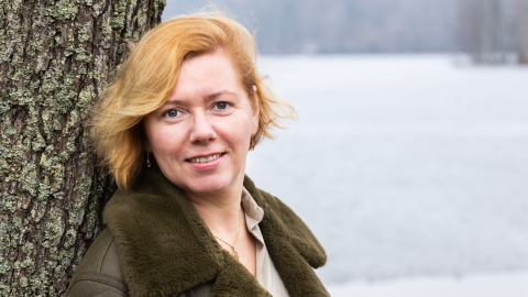 Henkilö nojaa puunrunkoon ja katsoo suoraan kameraan.