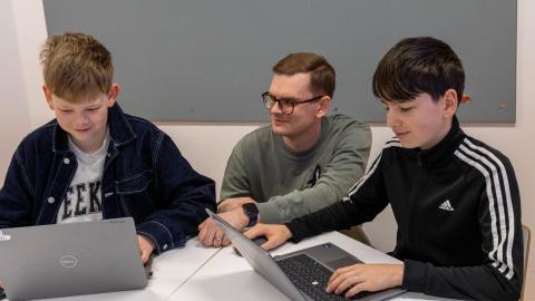 Aleksi Huttu opastaa pöydän ääressä olevaa kahta oppilasta Digimallien käytössä.