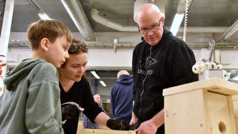 Kaksi aikuista ja yksi lapsi tarkkailevat, mikä vaihe pöntönrakennuksessa alkaa seuraavaksi.