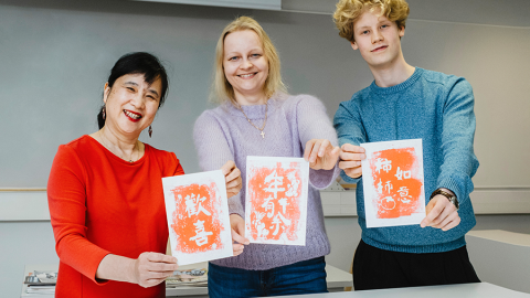 Three people stand in the classroom and show papers with Chinese characters on them.