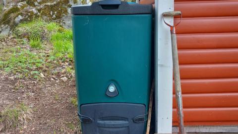 Vihreä biojätekompostori talon nurkalla.