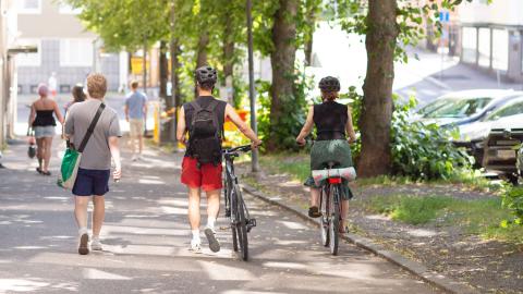 Kävelijöitä ja pyöräilijöitä Tampereen keskustassa, taustalla pysäköityjä autoja.