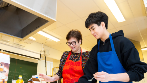 Kaksi henkilöä on leivontatarvikkeiden ääressä esiliinat edessään.