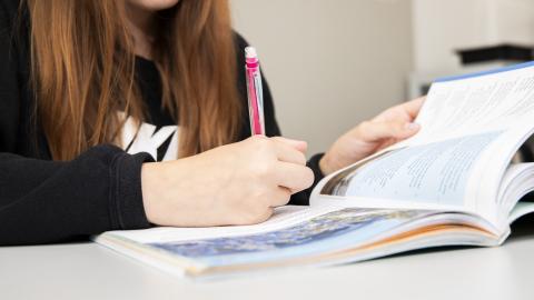 Avoinna oleva koulukirja etualalla, koululainen kirjoittaa siihen