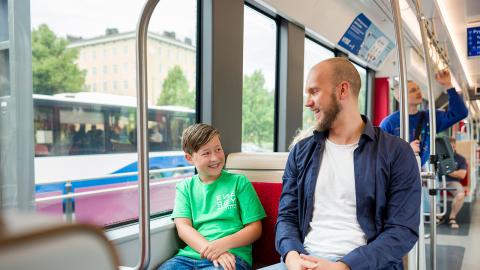 Mies ja poika istuvat bussissa, jonka ikkunasta näkyy tinen bussi.