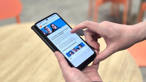 Close-up of the hands holding the phone. The phone screen shows the Tampere Residents' Panel website.
