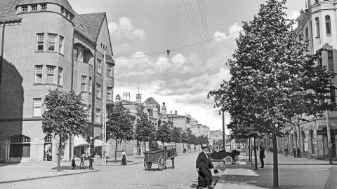 A quiet summer evening at the intersection of Hämeenkatu and Kuninkaankatu in 1913. City residents are getting around on foot, by horse, or by taxi. On the left is the Blom House, and on the right is the Pulla-Helin House. 