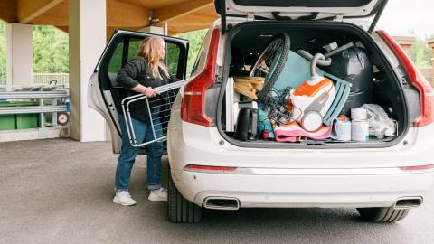 Henkilö lastaa autoa täyteen tavaraa ja auton takakontti on auki.