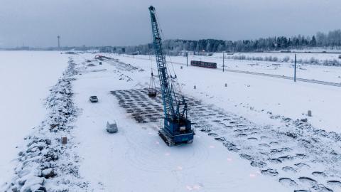 Kuvassa syvätiivistyspainoa pudottava kone louhesaarella, talvimaisemassa.