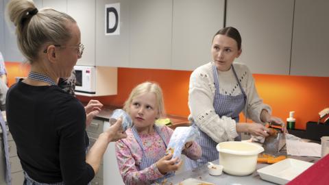 Kotitalousopettaja neuvoo äitiä ja tytärtä Perheköksässä kasviruoan tekemisessä.