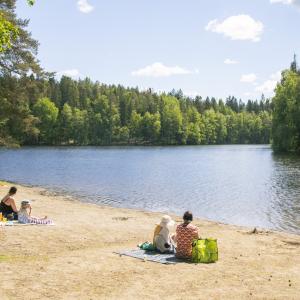 Ihmisiä uimarannalla istumassa hiekalla aurinkoisena päivänä.