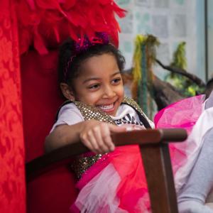 Child sits on a red chair and laughs.