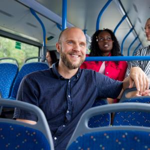 Mies istuu hymyillen bussin kyydissä.