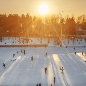 Luistelijoita Sorsapuiston tekojäällä, aurinko paistaa matalalta.